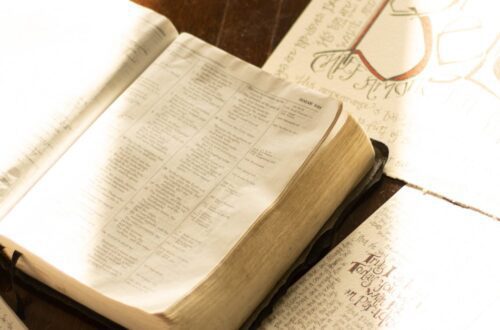 Open Bible with hand-drawn illustrations on a rustic wooden table, bathed in warm light.